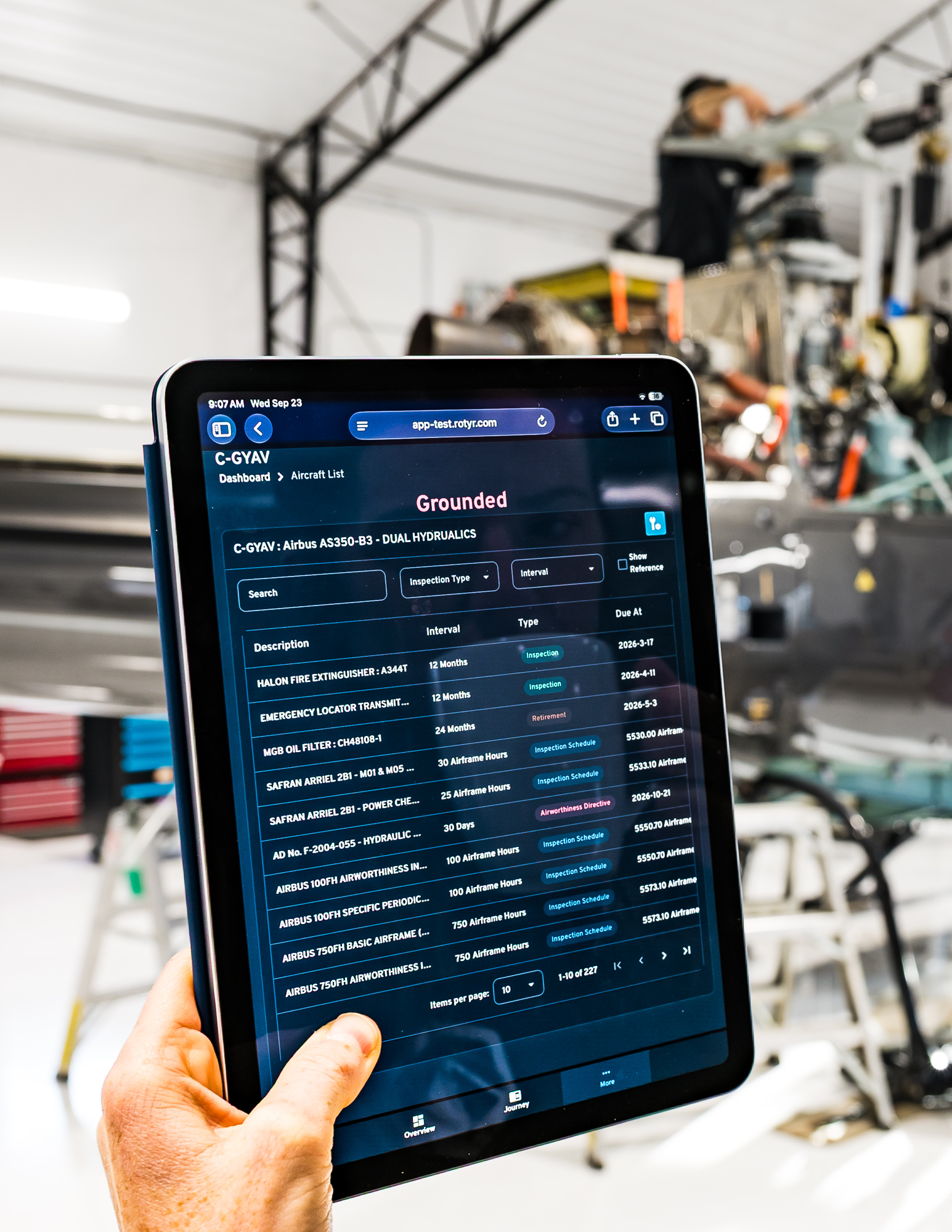 Technician holding a tablet displaying the ROTYR maintenance forecasting dashboard in a helicopter hangar